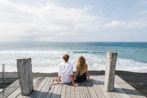 Couple in love sits on the dock and looks at the ocean, Bali.
