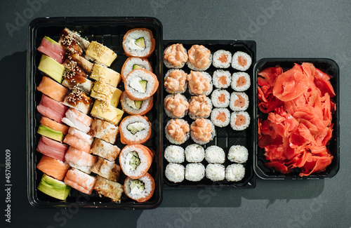 Japanese food concept. Catering, various kinds of sushi on plate. Placed on stone black background in plastic delivery box. Sushi roll (Philadelphia) with salmon, smoked eel, avocado, cream cheese. photo