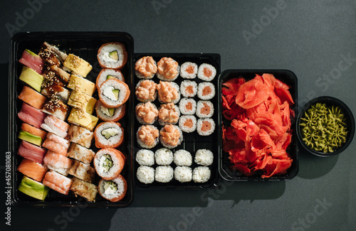 Japanese food concept. Catering, various kinds of sushi on plate or platter set. Chopsticks, ginger, soy sauce, wasabi. Placed on stone black background in plastic delivery box. photo