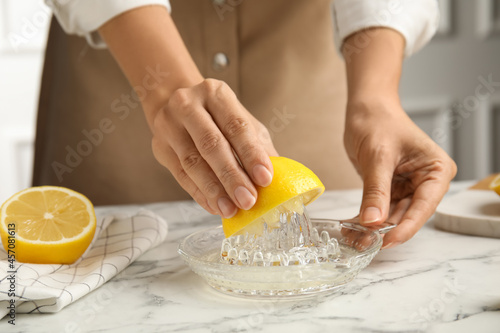 Fotografie Woman squeezing lemon juice at white marble table, closeup