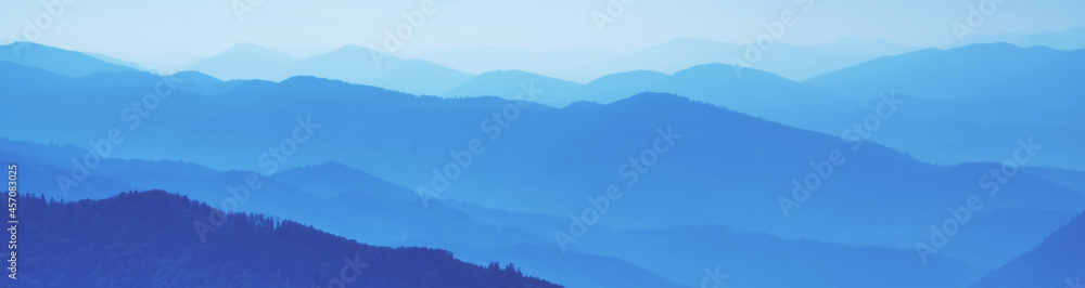 High peaks of beautiful blue mountain range landscape with fog and forest. Ukraine, Carpathians. Horizontal image.