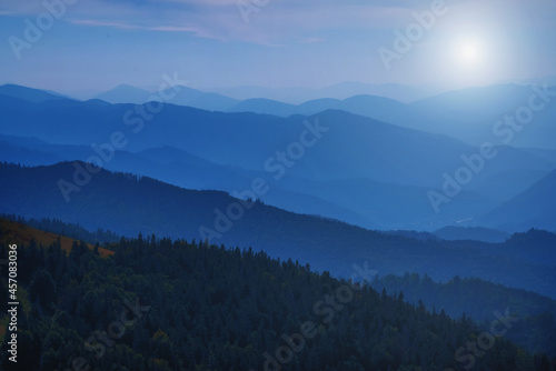 High peaks of beautiful dark blue mountain range landscape with fog and forest. Ukraine, Carpathians. Horizontal image.