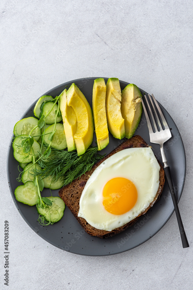 Delicious breakfast with avocado, fresh cucumbers and microgreens of peas with dill, fried eggs on black grain toast, top view Delicious breakfast with avocado, fresh cucumbers and microgreens of peas with dill, fried eggs on black grain toast, top view