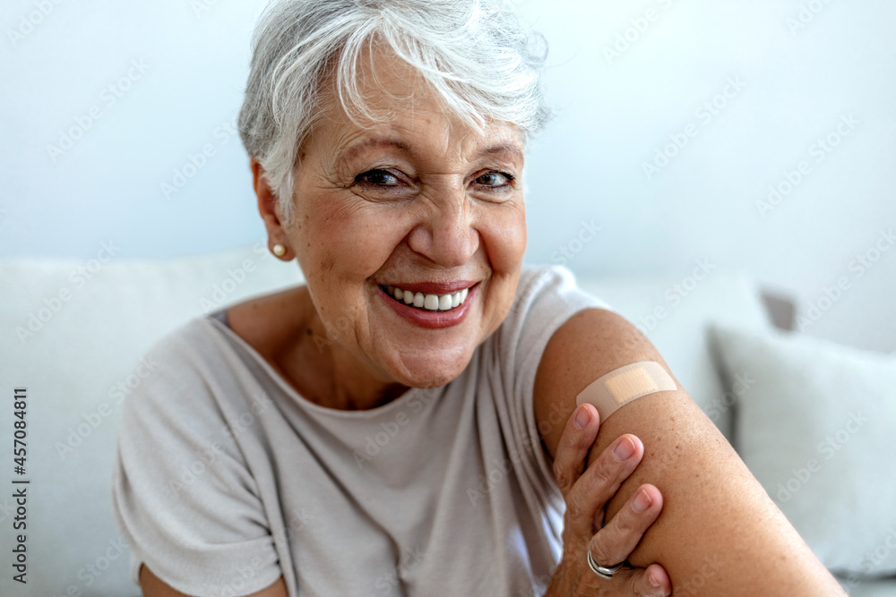 Proud mature woman smile after vaccination with bandage on arm. Beautiful smiling senior woman 70s after receiving the coronavirus vaccine. Elderly lady getting immunization via anti-viral vaccine. - obrazy, fototapety, plakaty 