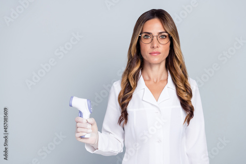 Photo of pretty confident lady doctor wear white coat holding non-contact thermometer empty space isolated grey color background