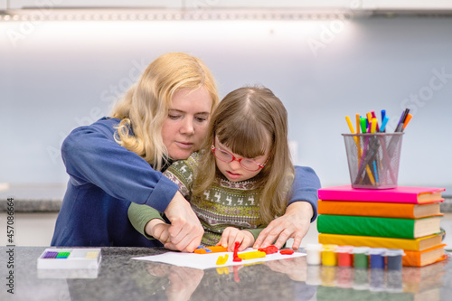 A girl with down syndrome sits next to her mother and is engaged in creativity. Education for people with disabilities concept