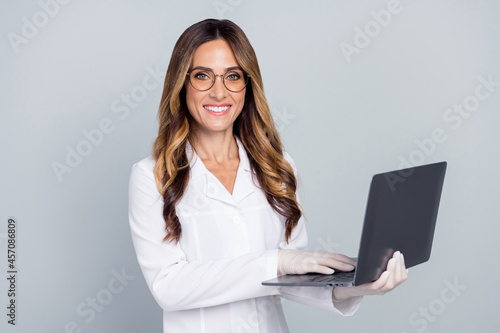 Photo of young nice brown hairdo lady write laptop wear eyewear gloves white nurse coat isolated on grey background