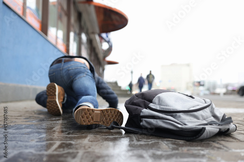 Man with backpack lying on slippery sidewalk after fall closeup