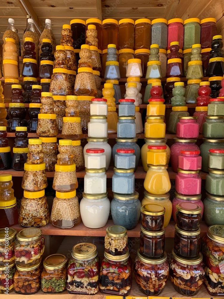 There are many jars of organic, natural honey on the counter for sale. Different honey, different colors in plastic cans are ready for sale at the honey fair. Nuts filled with honey. There are many jars of organic, natural honey on the counter for sale. Different honey, different colors in plastic cans are ready for sale at the honey fair. Nuts filled with honey.