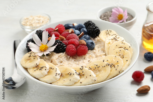 Tasty oatmeal porridge with berries, banana and chia seeds served on light wooden table, closeup
