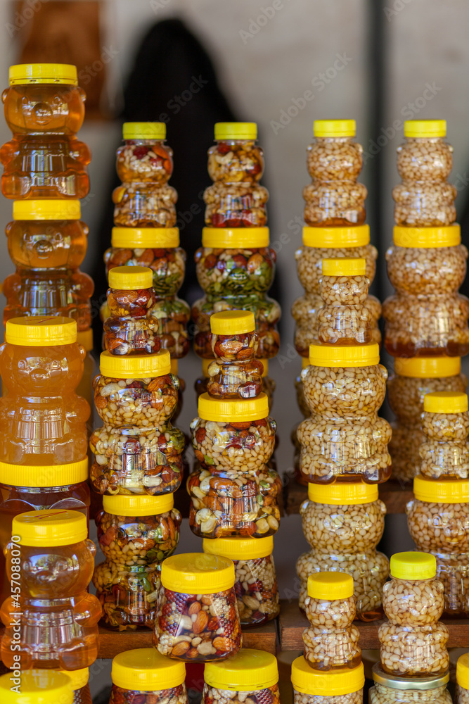 There are many jars of organic, natural honey on the counter for sale. Different honey, different colors in plastic cans are ready for sale at the honey fair. Nuts filled with honey. 