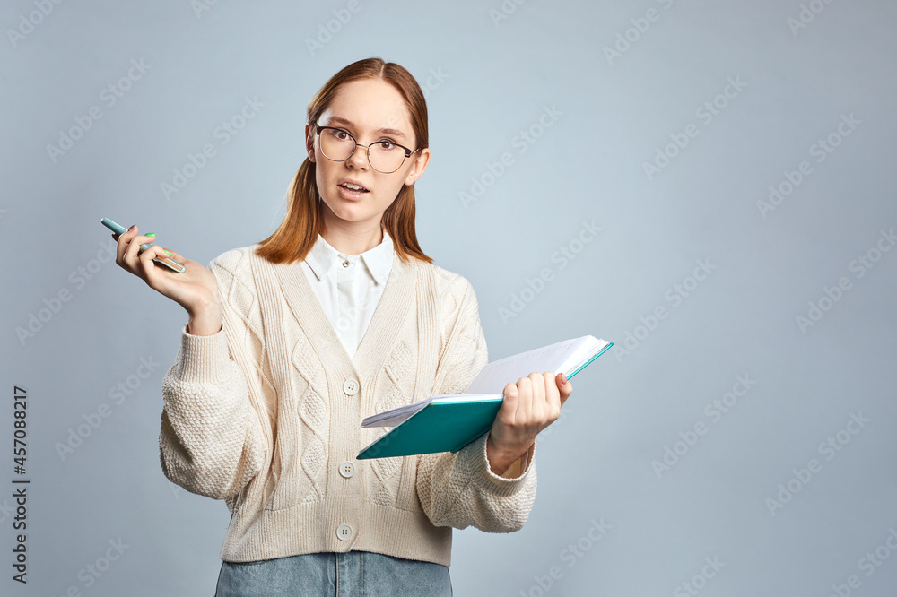amazed young girl wearing casual sweater talking on cellphone while read notebook. Cute female student using phone and holding book in hands. Studio shot. amazed young girl wearing casual sweater talking on cellphone while read notebook. Cute female student using phone and holding book in hands. Studio shot.