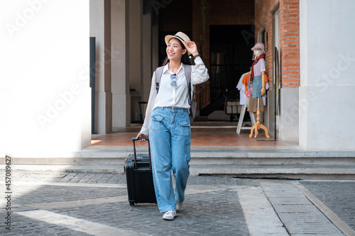 Asian woman tourist is traveling on holiday trip with hat and dragging her black luggage