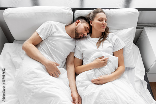 rest and people concept - happy couple sleeping in bed at home