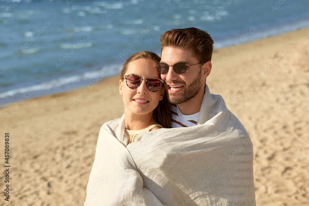 leisure, relationships and people concept - happy couple in sunglasses covered with blanket hugging on summer beach leisure, relationships and people concept - happy couple in sunglasses covered with blanket hugging on summer beach
