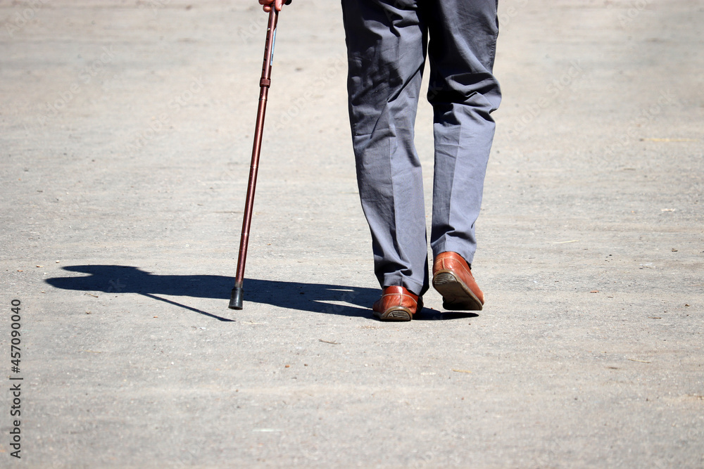 Man walking with a cane on a street, male legs in trousers on sidewalk. Concept of disability, limping person, diseases of the spine, old people Man walking with a cane on a street, male legs in trousers on sidewalk. Concept of disability, limping person, diseases of the spine, old people