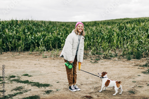 Cheerful teenage girl playing in the field with her dog Jack Russell Terrier on the background of a corn field in autumn photo