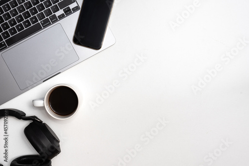 Copy space flat lay of white desk with office supplies at left side, tecnologic and comunication media. Workspace. White background laptop, headphpones, smartphone, coffee, notebook photo