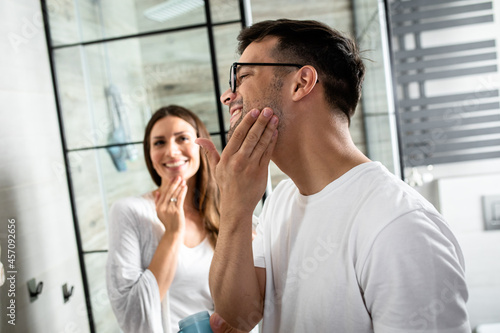 Young couple going through morning routine in the bathroom applying face cream.