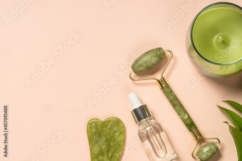 Fototapeta Naklejka Na Ścianę i Meble -  Cosmetic products - Jade roller and gua sha massager with cream and serum bottles at pastel background. Spa background. Top view with copy space.