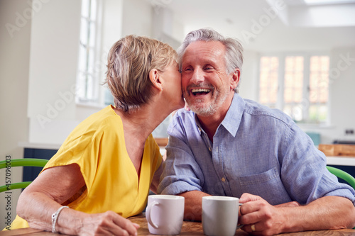 Loving Retired Couple Sitting Around Table At Home Having Morning Coffee Together