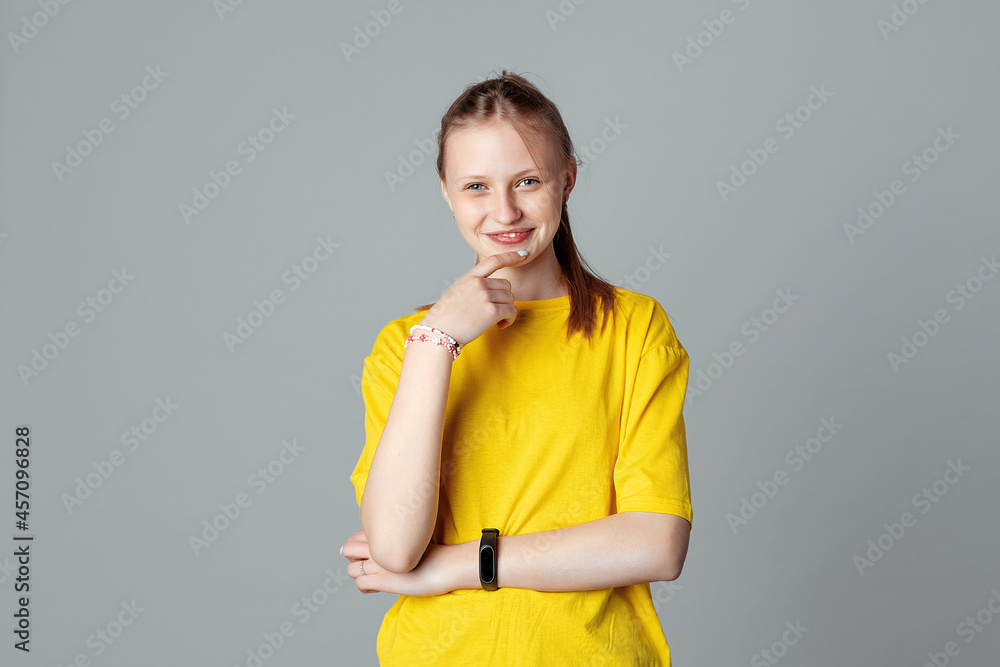 Smiling teen girl looking at the camera touching herself face by index finger isolated on light grey background. Thinking positive Smiling teen girl looking at the camera touching herself face by index finger isolated on light grey background. Thinking positive