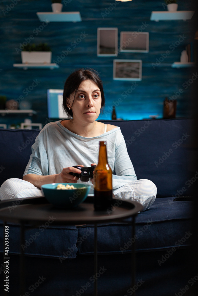Angry disappointed woman holding gaming joystick playing soccer video games on TV losing online videogames competition. Frustrated expressive person drressing in pajama relaxing late night