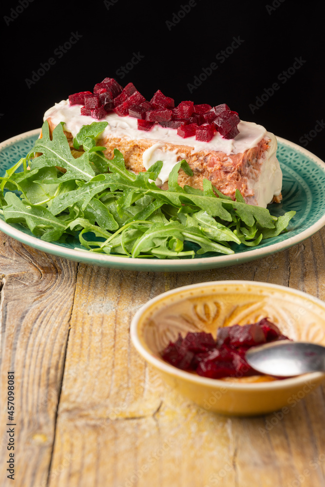 Top view of cod pudding with mayonnaise and arugula, bowl with beetroot, selective focus, on rustic wooden table, black background, vertical Top view of cod pudding with mayonnaise and arugula, bowl with beetroot, selective focus, on rustic wooden table, black background, vertical