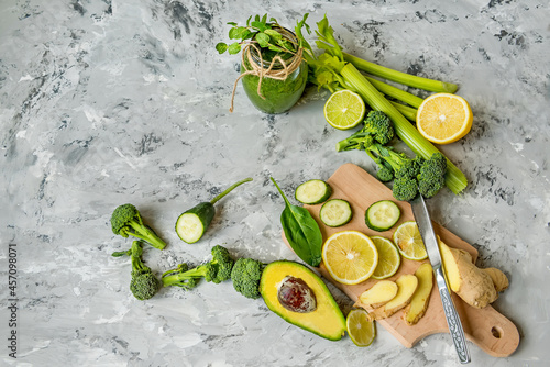 Brocoli, cucumber lemon ginger - green vegetable ingredients for a healthy smoothie. different vegetables on a gray concrete background and a green smoothie. View from above.