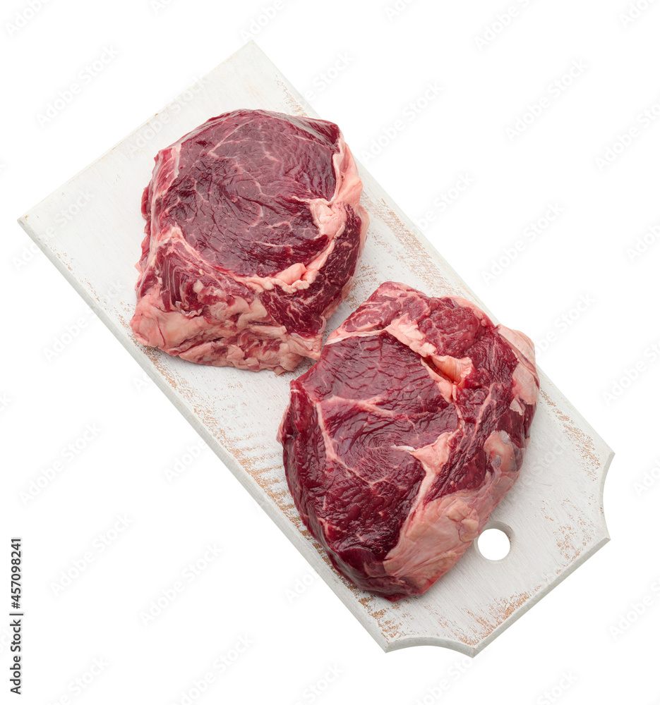 raw piece of beef ribeye with rosemary, thyme on a white background raw piece of beef ribeye with rosemary, thyme on a white background