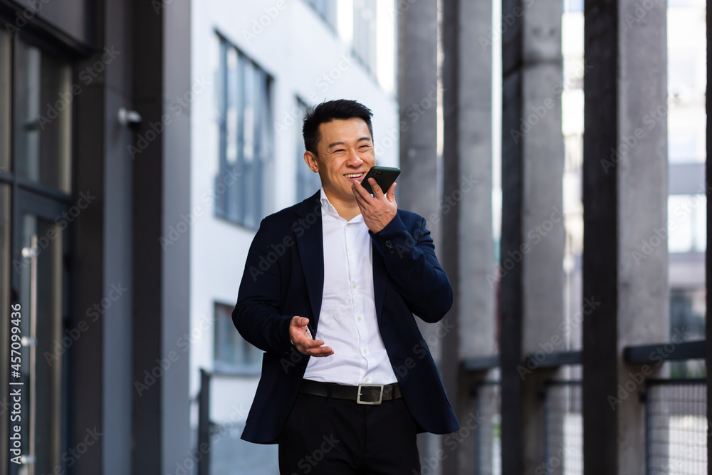 cheerful smiling Successful Asian businessman explains information to employees using phone, speaks near office outside happy talking cheerful smiling Successful Asian businessman explains information to employees using phone, speaks near office outside happy talking