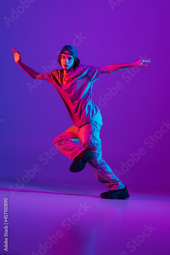 Stylish sportive boy dancing hip-hop in stylish clothes on colorful background at dance hall in neon light. Youth culture, movement, style and fashion, action.