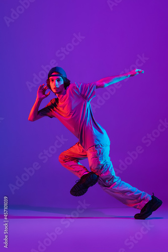 Young stylish man, break dancing, hip-hop dancer practicing solo in casual clothes isolated over purple background in neon pink light at dance hall