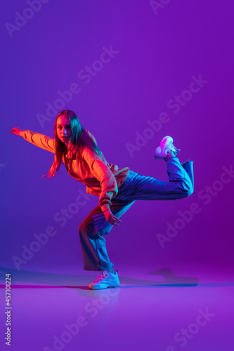 Stylish sportive girl dancing hip-hop in stylish clothes on colorful background at dance hall in neon light. Youth culture, movement, style and fashion, action.