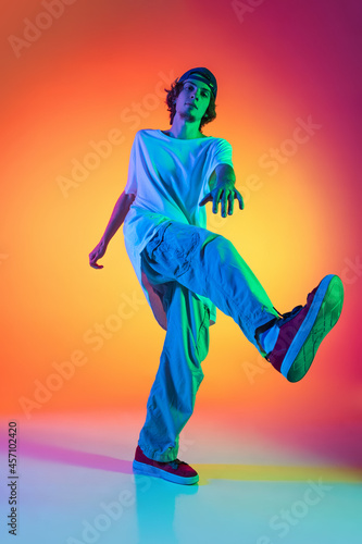 Close-up portrait of young man, hip-hop dancer in stylish clothes in action isolated on colorful background at dance hall in neon light.