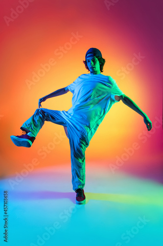 Conceptual portrait of young man, hip-hop dancer in stylish clothes in action isolated on colorful background at dance hall in neon light. © master1305