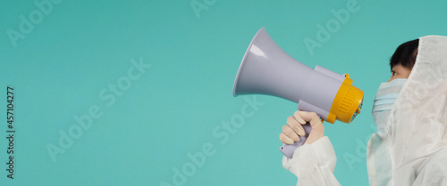 Hand hold megaphone.Asian woman wear PPE suit and face mask on mint green or Tiffany Blue background.