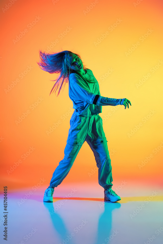 One Caucasian sportive girl dancing hip-hop in stylish clothes on colorful background at dance hall in neon light. Youth culture, movement, style and fashion, action.