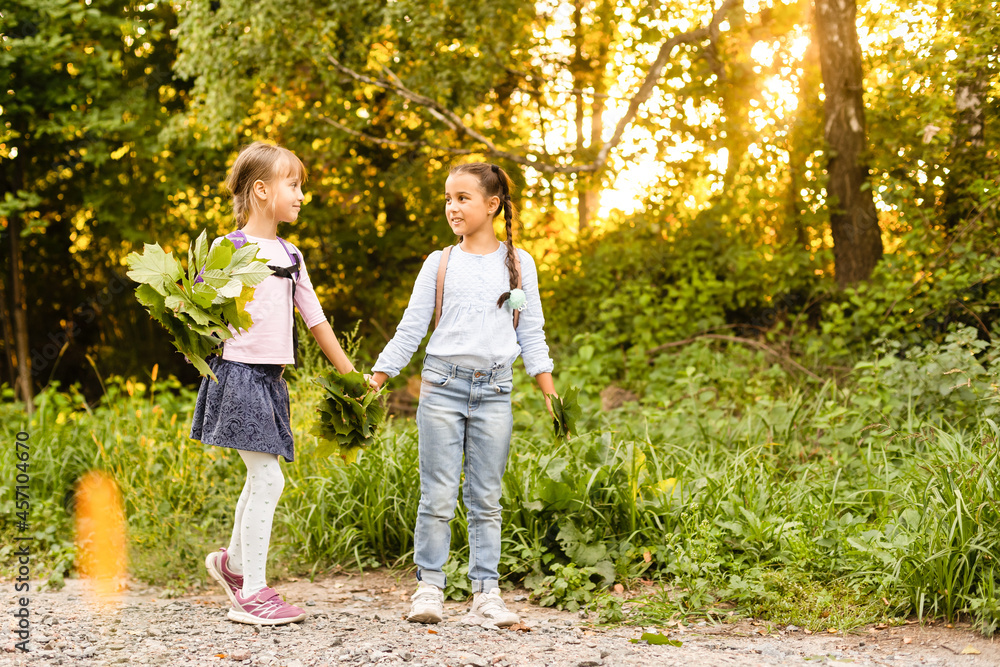 Fototapeta premium Two girls are having fun in the park, autumn outfit. Funny girl friends throwing leaves in the city in autumn. Happy family on autumn walk. Geasture peace.