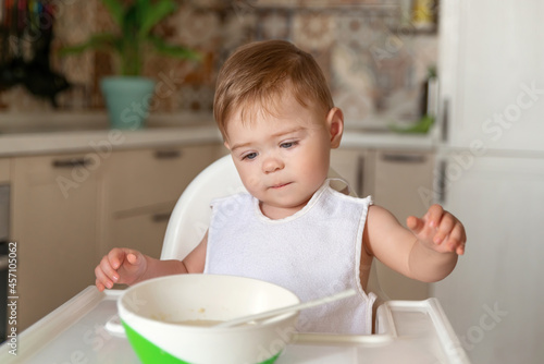 Happy cute infant baby boy eats itself. Caucasian little baby boy with funny face concentrated on food. Attempt to eat by himself. Child nutrition