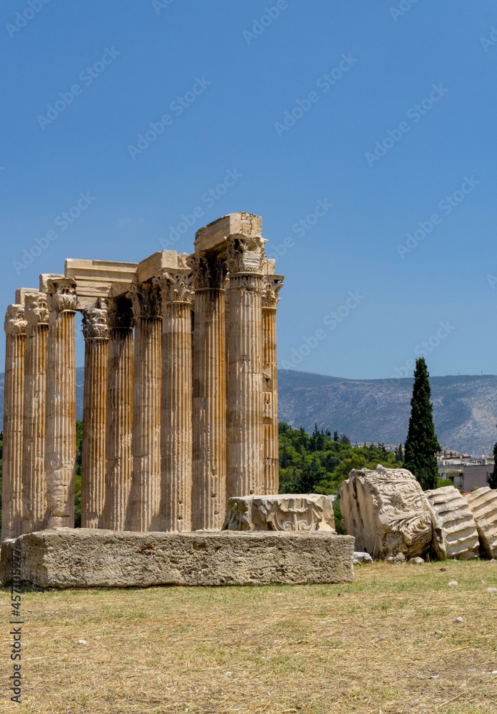 Greek-style columns, in ruins, with a blue sky and atop a green grass