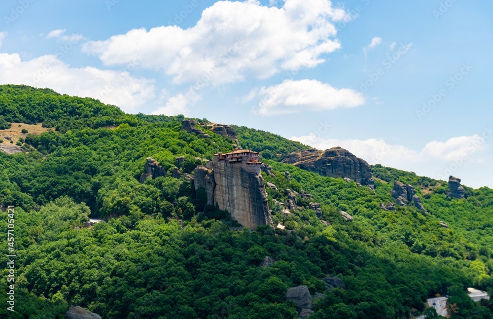 Meteora Monastery on top of the rock, with a green forest and a blue sky with white clouds