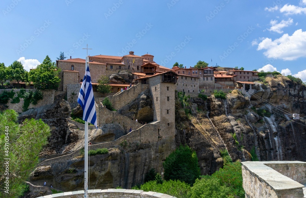 View of a Meteora monastery with its stairs from the other side of the mountain, with the flag of Greece in front
