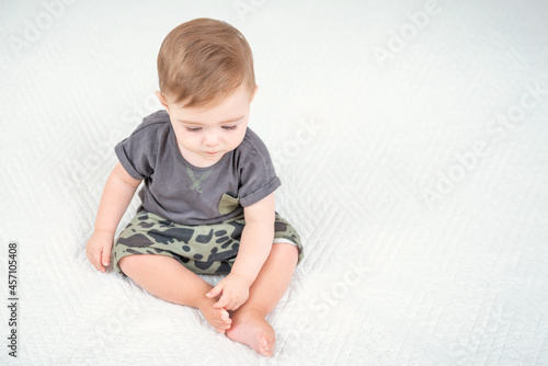Caucasian baby boy in a khaki shorts sitting on bed in room. View from top above. Healthy childhood lifestyle.