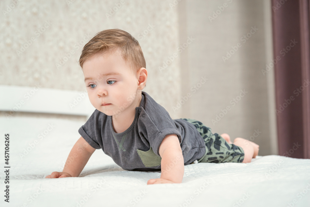 Front side view of blond haired pretty crawling baby on the bed on a white sheet in the parents bedroom. Serious child. Stay home Front side view of blond haired pretty crawling baby on the bed on a white sheet in the parents bedroom. Serious child. Stay home