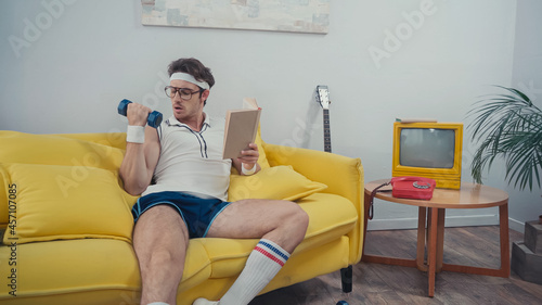 Sportsman lifting dumbbell while holding book in living room