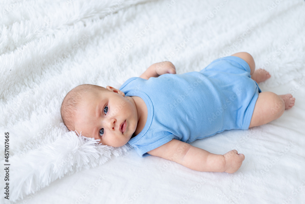cute baby boy three months old in a blue bodysuit on a white bed at home cute baby boy three months old in a blue bodysuit on a white bed at home