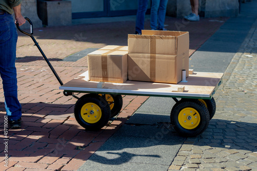Fotografie Luggage trolley with 4 wheels with brown boxes on street in city, Service deliver carrying packages to delivery to customer with low angle of peoples