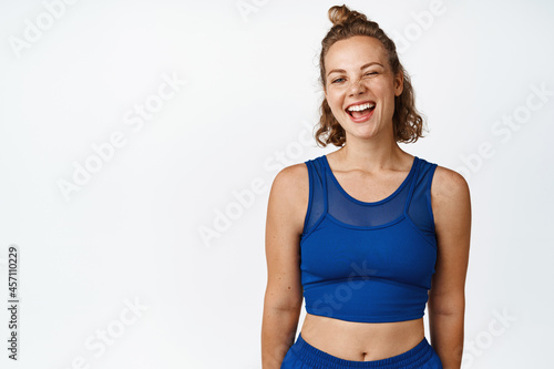 Portrait of happy sports woman winking, smiling and looking at camera, wearing blue activewear for fitness workout, white background