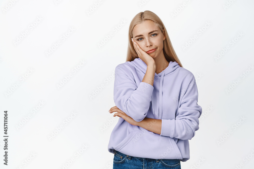 Sad and unamused blond woman smirking, looking at camera unimpressed, standing bored against white background Sad and unamused blond woman smirking, looking at camera unimpressed, standing bored against white background